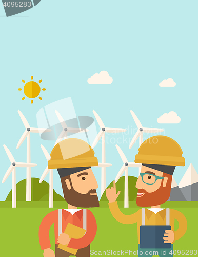 Image of Two workers talking infront of windmills.