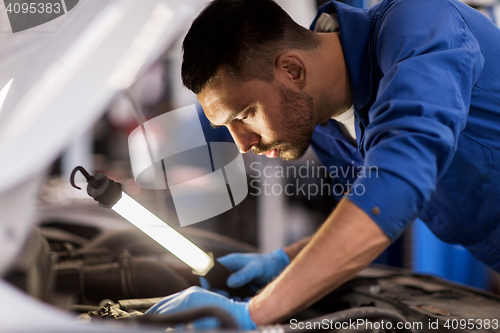 Image of mechanic man with lamp repairing car at workshop