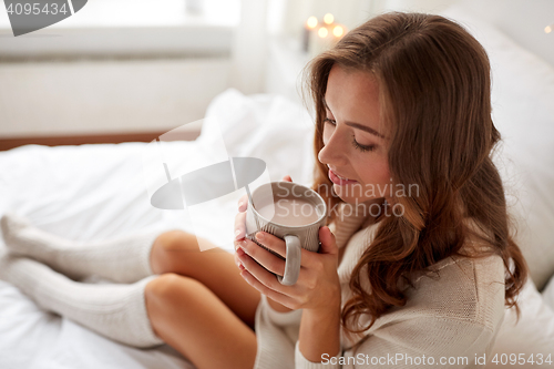 Image of happy woman with cup of cocoa in bed at home