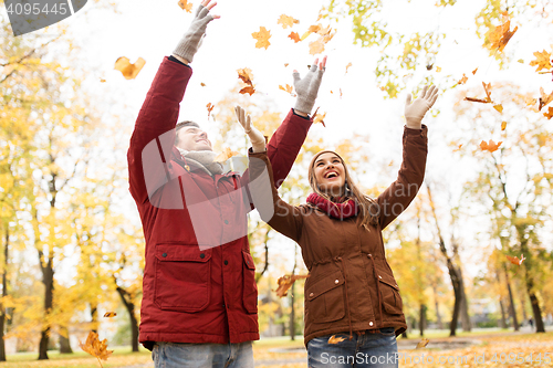 Image of happy young couple throwing autumn leaves in park