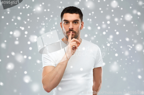 Image of young man making hush sign over snow background