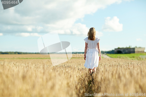 Image of young woman in white dress walking along on field