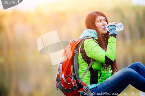 Image of Brunette drinking water with backpack sitting close-up