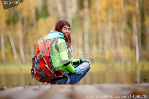 Image of Brunette with backpack sitting on bridge at lake