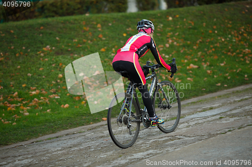Image of Sport young woman in tracksuit riding bicycle in early autumn