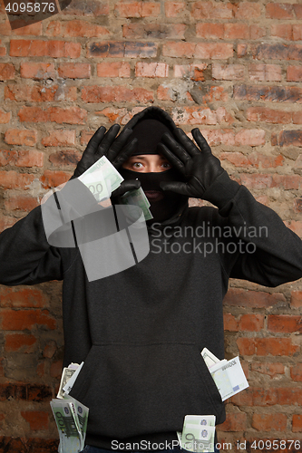 Image of Burglar with banknotes raises hands