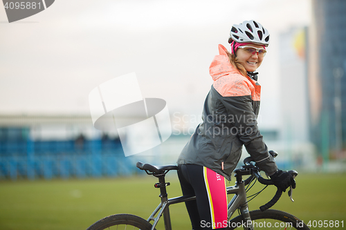 Image of Portrait of smiling female bicyclist in tracksuit outdoors