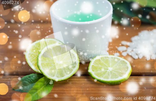 Image of citrus body lotion in cup and limes on wood