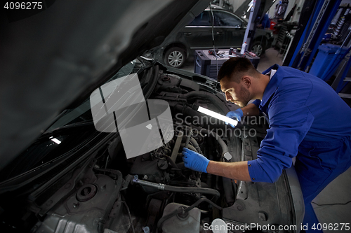 Image of mechanic man with lamp repairing car at workshop