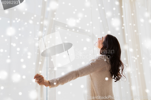 Image of pregnant woman opening window curtains