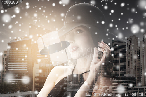 Image of woman in black hat over city background and snow