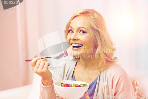 Image of smiling middle aged woman eating salad at home