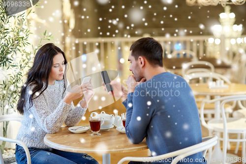 Image of couple with smartphones drinking tea at cafe