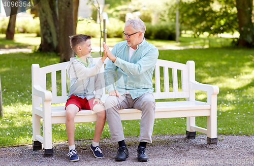 Image of old man and boy making high five at summer park