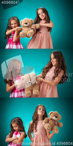 Image of The two cute little girls on blue background with Teddy bear