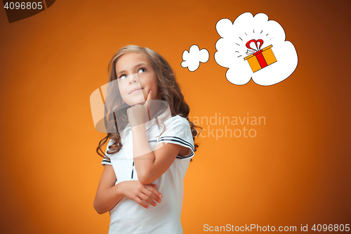 Image of The cute thoughtful little girl on orange background