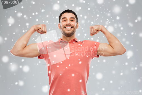 Image of smiling man showing biceps over snow background