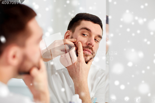 Image of man squeezing pimple at bathroom mirror