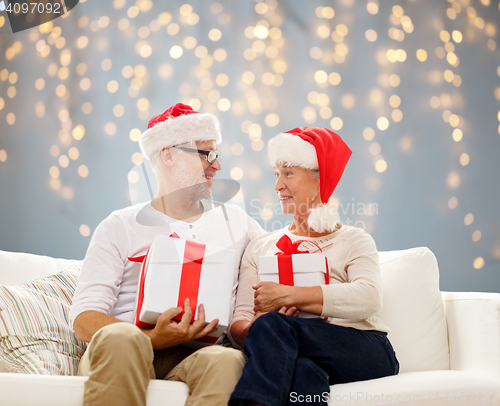 Image of happy senior couple in santa hats with gift boxes