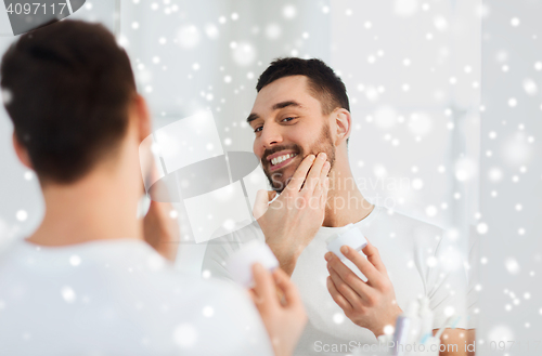 Image of happy young man applying cream to face at bathroom