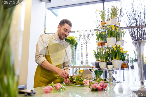 Image of smiling florist man making bunch at flower shop