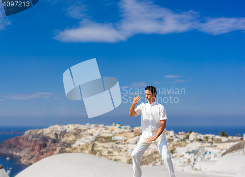 Image of Handsome man practicing Tai Chi of the rooftops in Oia Santorini