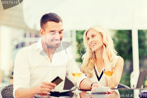 Image of happy couple with bank card and bill at restaurant