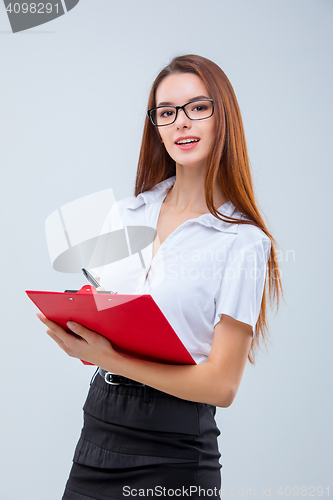 Image of The smiling young business woman with pen and tablet for notes on gray background