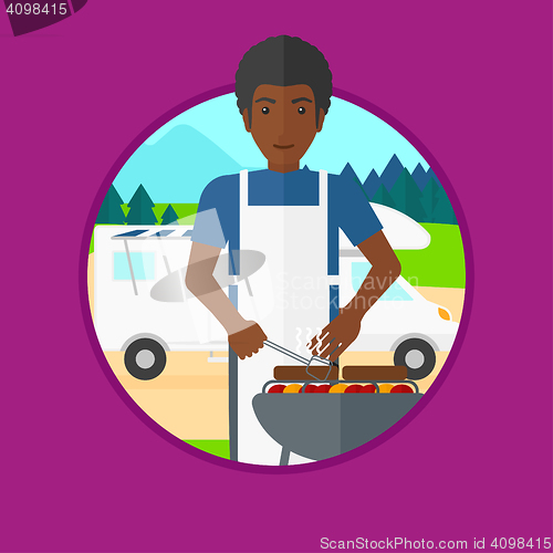 Image of Man having barbecue in front of camper van.