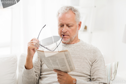 Image of senior man in glasses reading newspaper at home