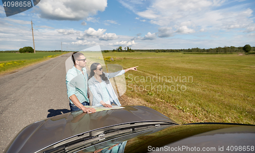 Image of happy man and woman with road map on car hood