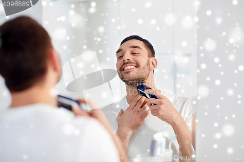 Image of man shaving beard with trimmer at bathroom