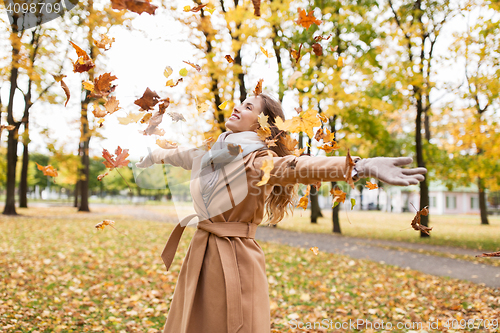 Image of happy woman having fun with leaves in autumn park