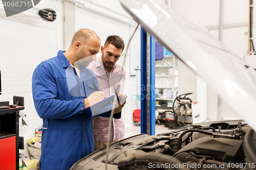 Image of auto mechanic with clipboard and man at car shop