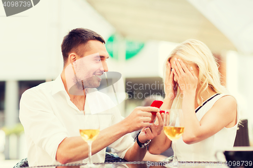 Image of happy couple with engagement ring and wine at cafe