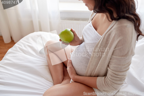 Image of close up of pregnant woman eating apple at home