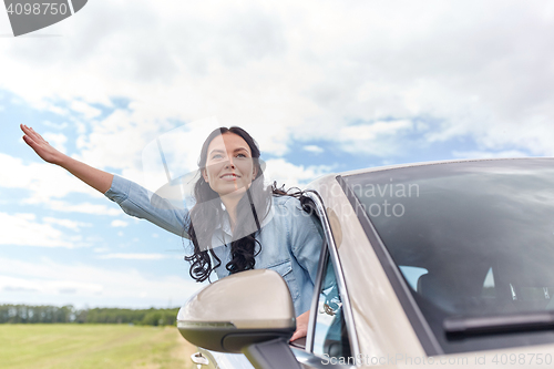 Image of happy young woman driving in car and waving hand