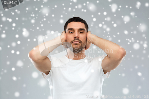 Image of young man covering his ears with hands over snow