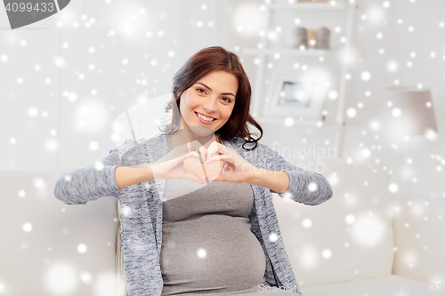 Image of happy pregnant woman making heart gesture at home