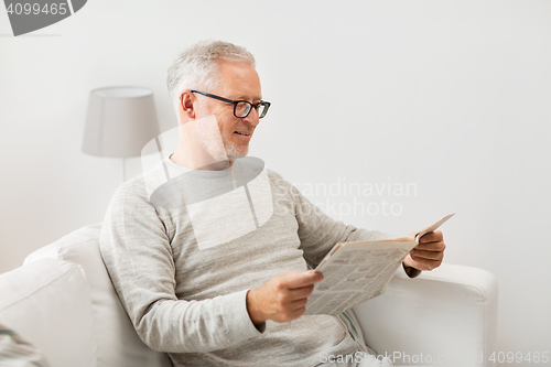 Image of senior man in glasses reading newspaper at home