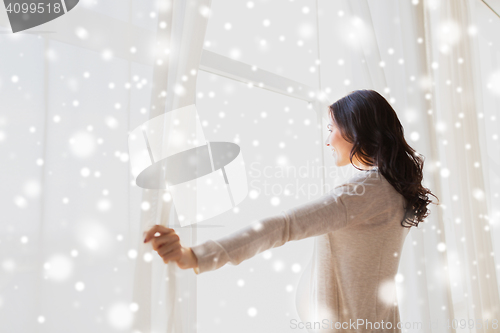 Image of close up of pregnant woman opening window curtains