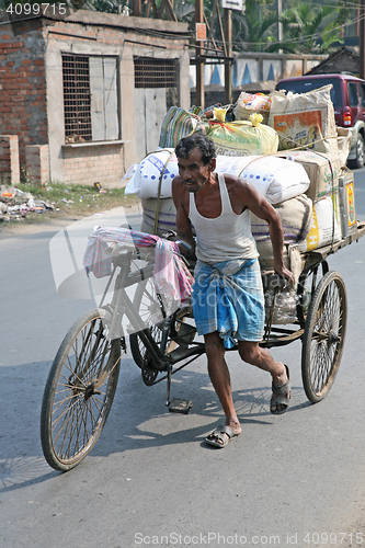 Image of Man pushing heavily loaded cycle rickshaw through the streets of, Baruipur, India