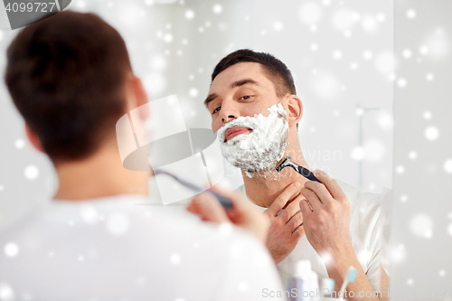 Image of man shaving beard with razor blade at bathroom