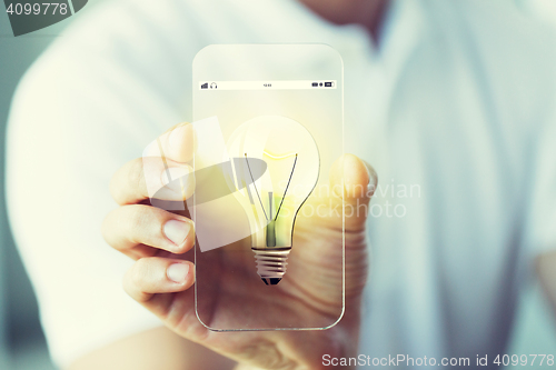 Image of close up of hand with light bulb on smartphone