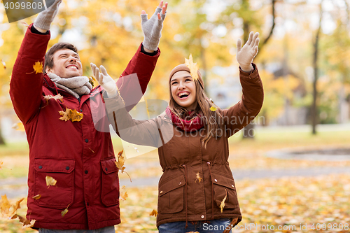 Image of happy young couple throwing autumn leaves in park