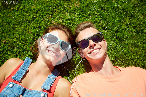 Image of happy teenage couple with earphones lying on grass