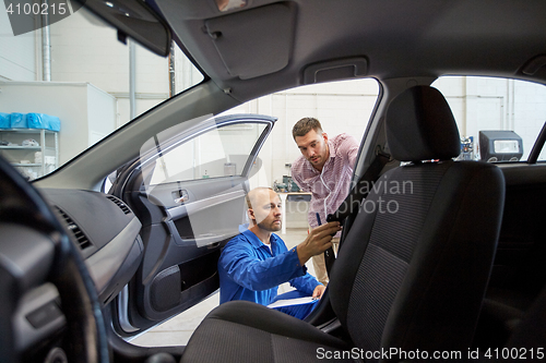 Image of mechanic and man checking seat belt at car shop