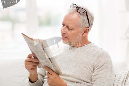 Image of senior man in glasses reading newspaper at home