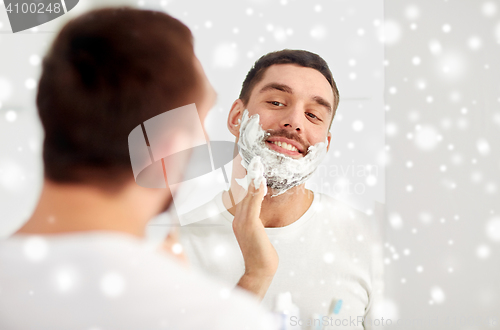 Image of happy man applying shaving foam at bathroom mirror