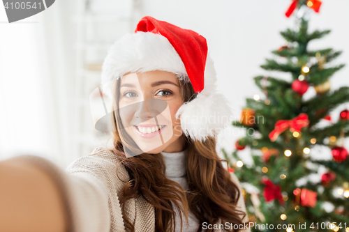 Image of happy woman in santa hat over christmas tree